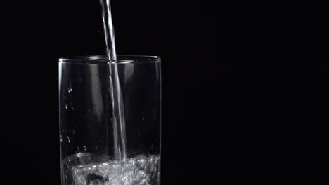 pouring fresh mineral still water into glass on a table. fresh sparkling drink with oxygen balls on black background