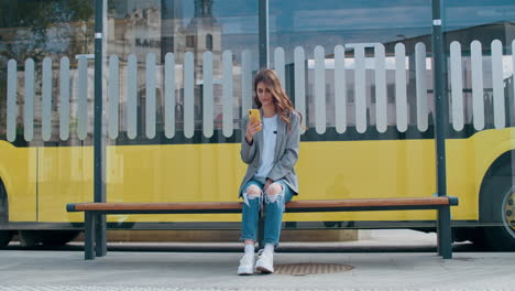 young woman using smartphone while waiting at a bus stop