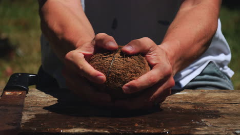 Close-up-of-man-holding-coconut,-cutting-it-in-half-with-machete