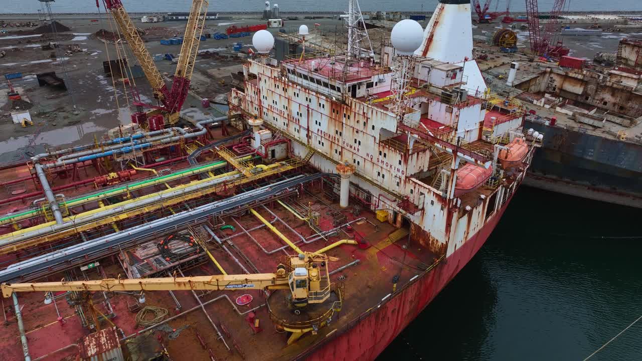 Drone footage of an old red tanker with a rust-covered hull. Corrosion and weathering are visible on the ship's sides and walls, showing signs of decay and abandonment.