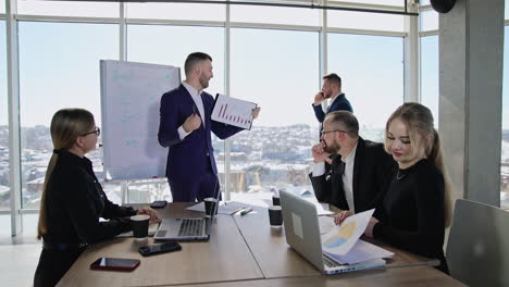 collaborative business team gathered at the table to discuss the strategies. man in suit showing charts to the colleague. male speaking on the phone at the backdrop.