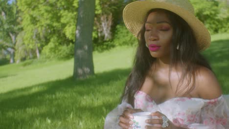 Black-Woman-drinking-tea-adjusting-hair-in-park-picnic-close-up