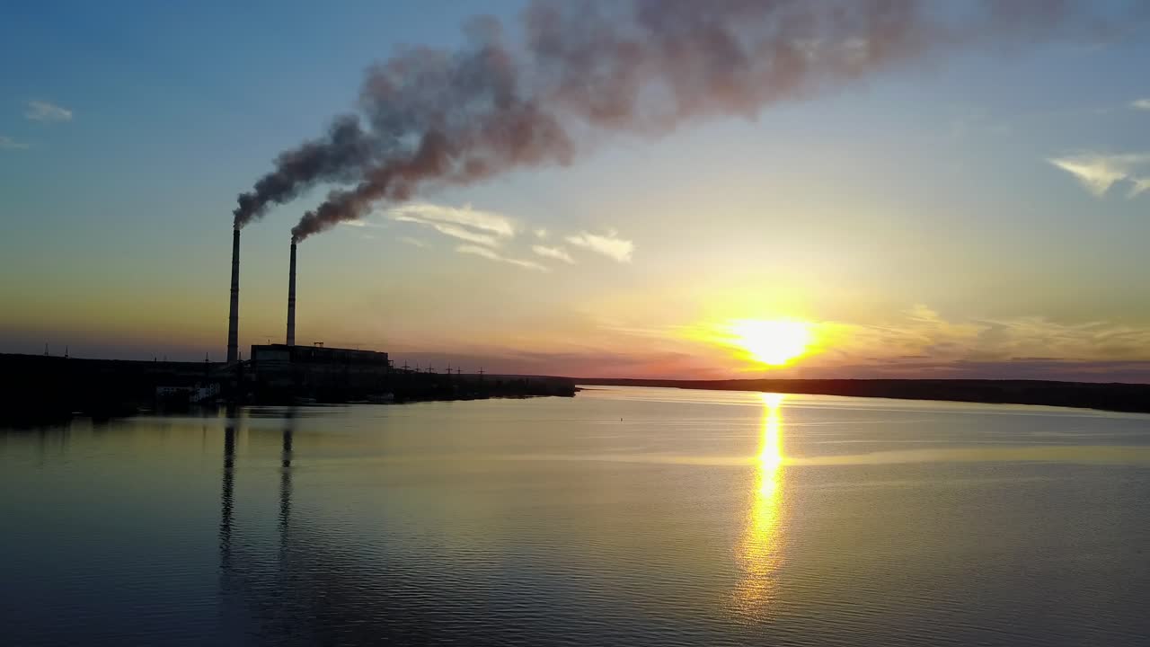 Power station with pipes of which poured smoke on a river at sunset