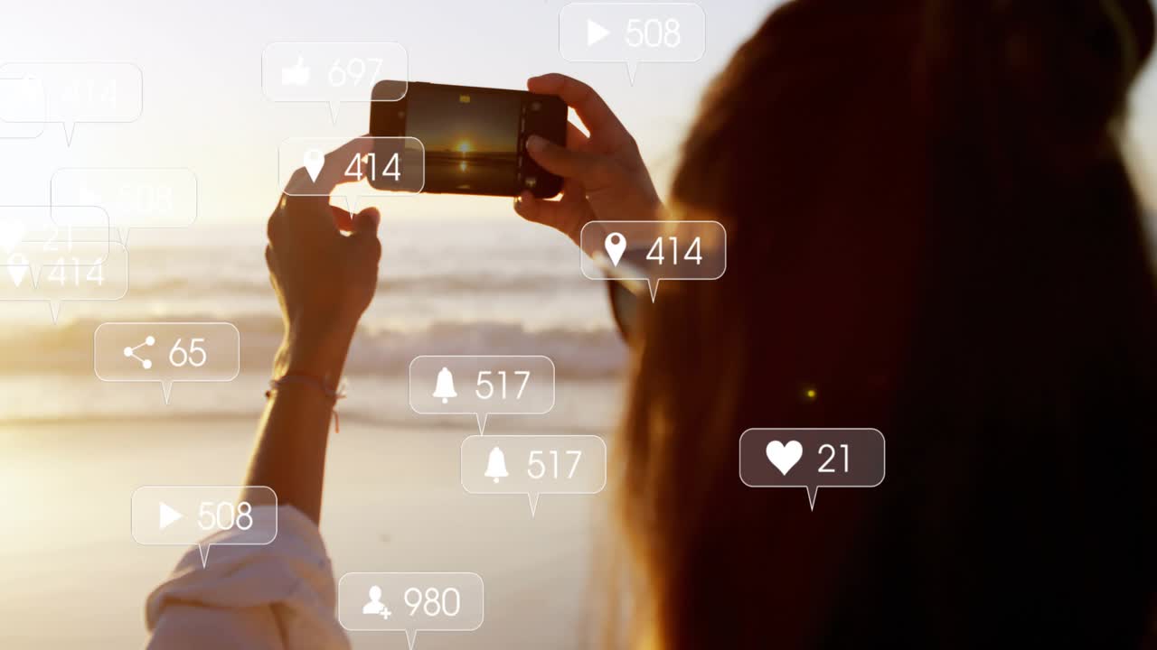 woman raising phone on beach framing sunset for social media, generating badges drifting right