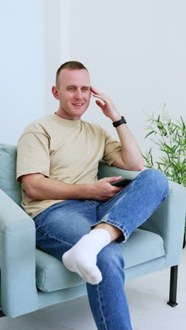 Relaxed Caucasian man sitting in the armchair uses his smartphone. Spending free time with gadgets and internet. Vertical video.