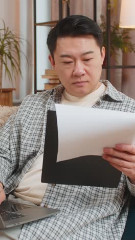 chinese male accountant using laptop working with financial graph documents reports of home income
