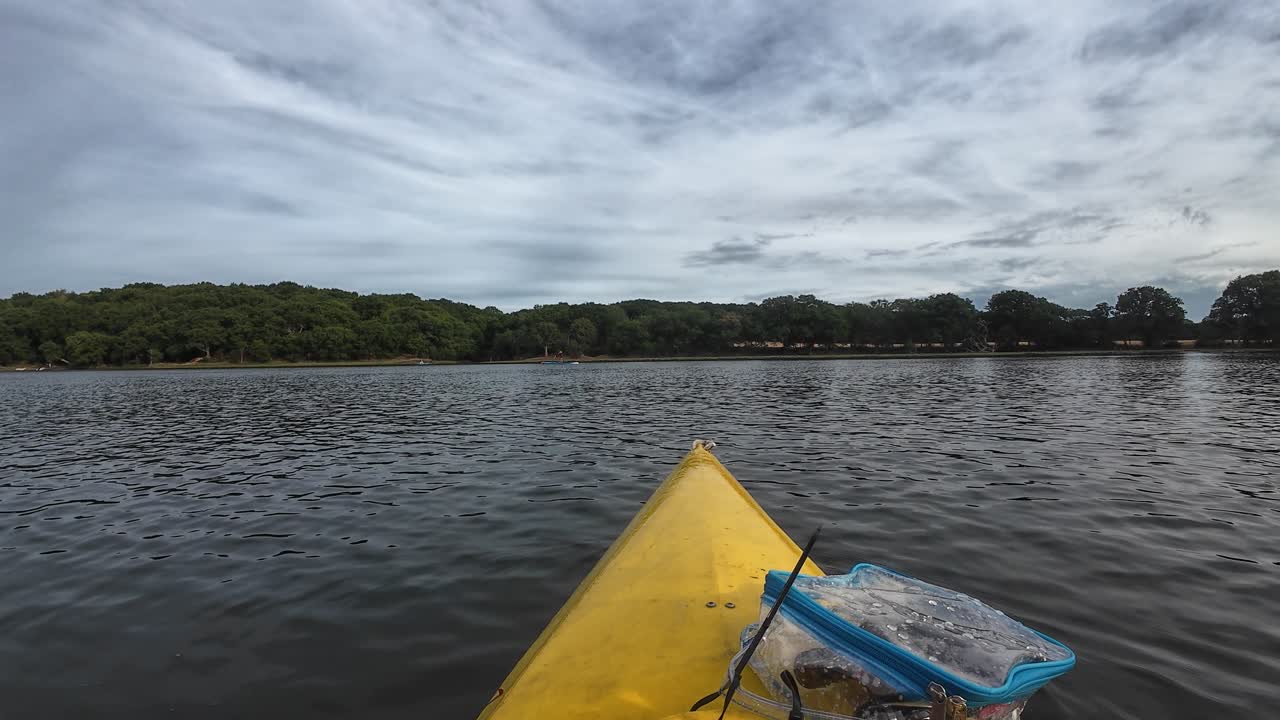 Kayaking on the calm waters of Hamble River in southern England. The yellow kayak cuts through serene waters, with green trees lining the riverbanks and the sky overhead