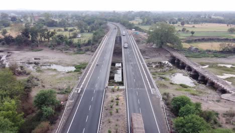 drone coming down to establish a generic looking well maintained national highway of india with rural landscape of farmlands and river with heavy commercial goods carrier trucks driving by