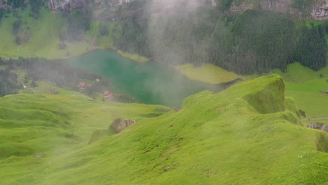 Downward-angle-drone-shot-of-a-mountain-ridge-revealing-a-lake-a-few-small-buildings-located-in-the-canton-of-Appenzell-Innerrhoden-in-Switzerland