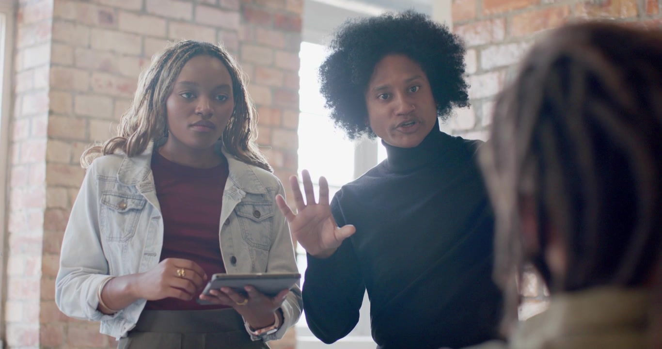 African American team standing in office one holding tablet other in turtleneck gesturing answering