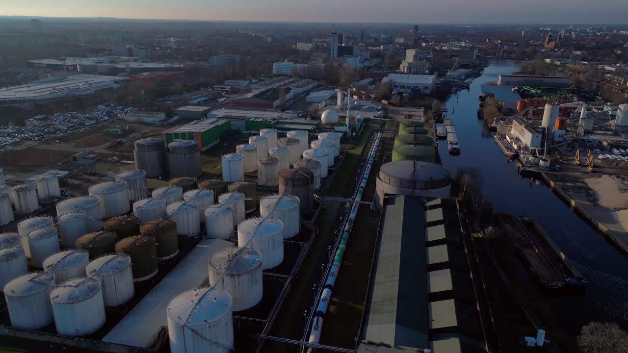 Berlin biogas plant with its large white tanks reflecting on the river next to it during sunset. Wonderful aerial view flight fly reverse drone