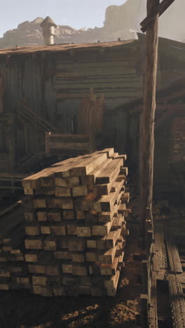 a pile of wood stacked in front of an old wooden building in a dusty, rural setting