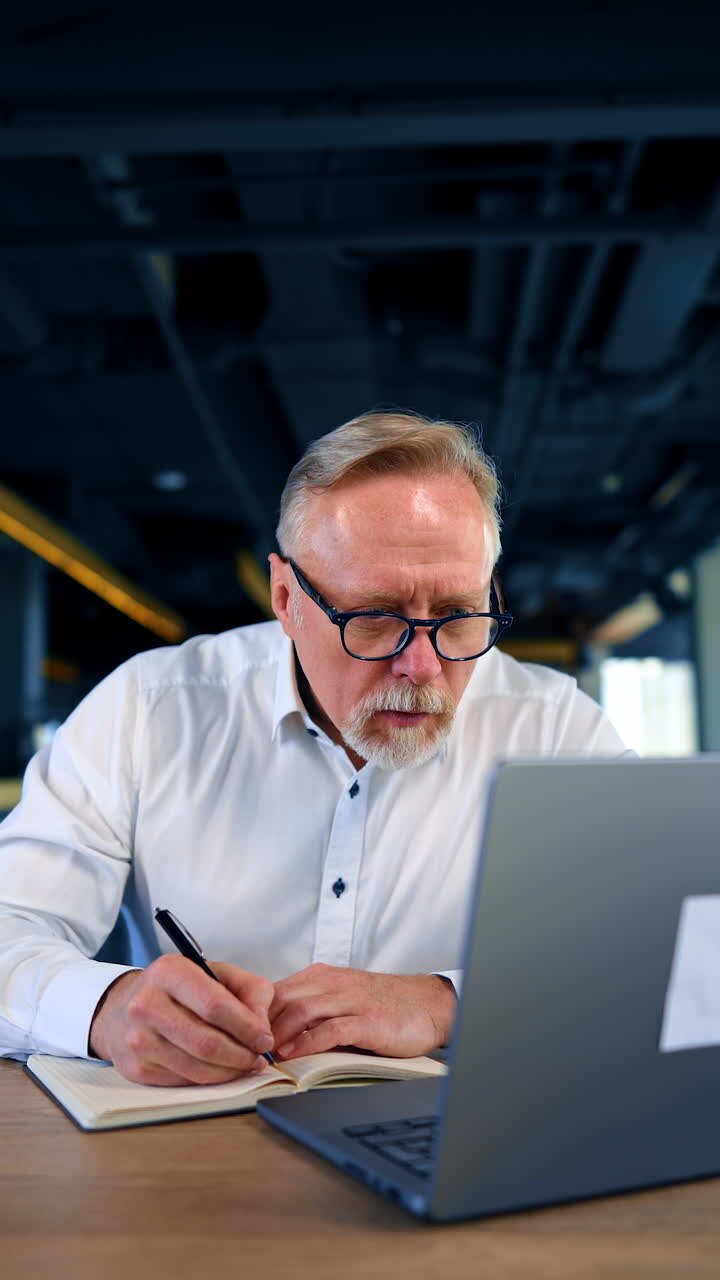 Focused male businessman looks at his laptop attentively. Man looks at computer screen unable to believe his own eyes. Vertical video.