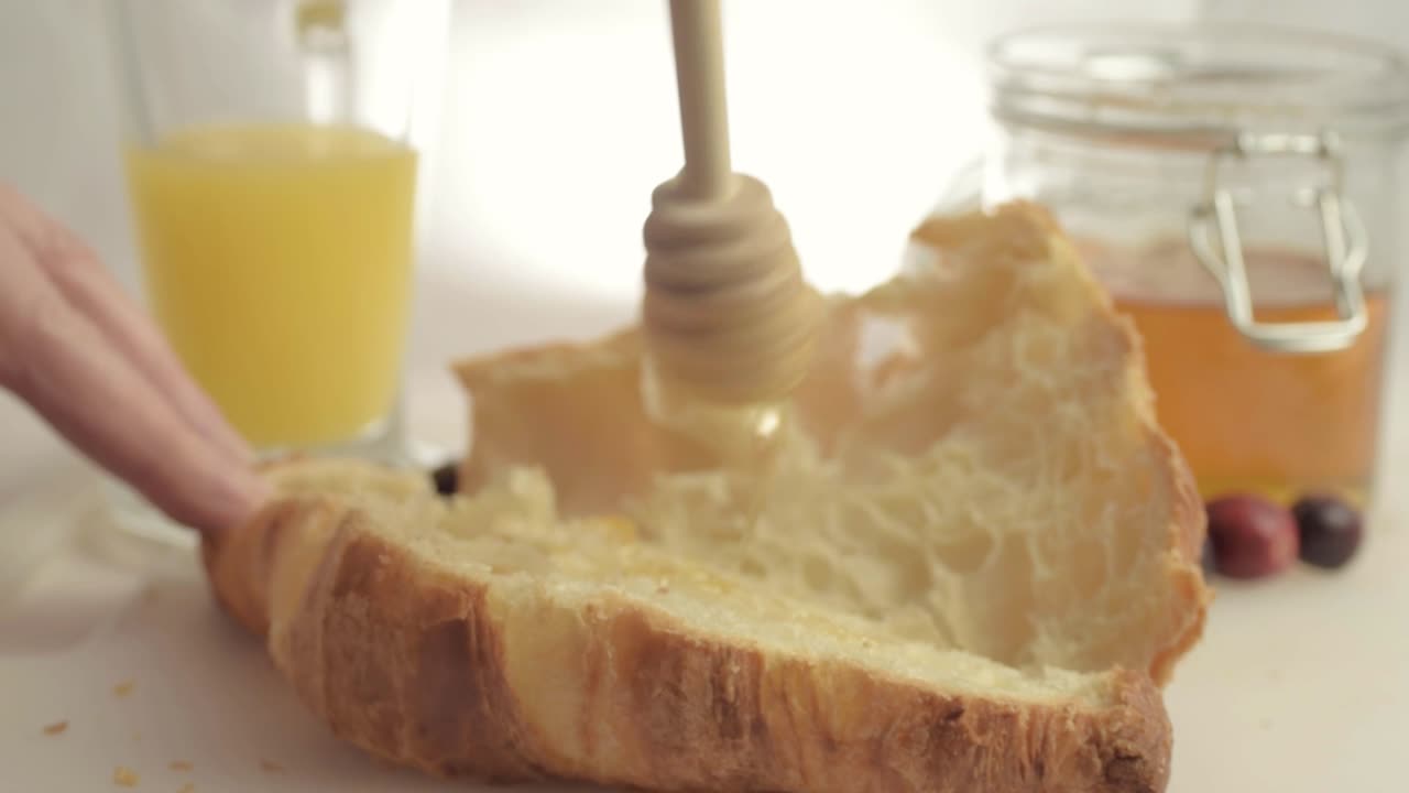 Drizzling honey on fresh baked croissant medium shot