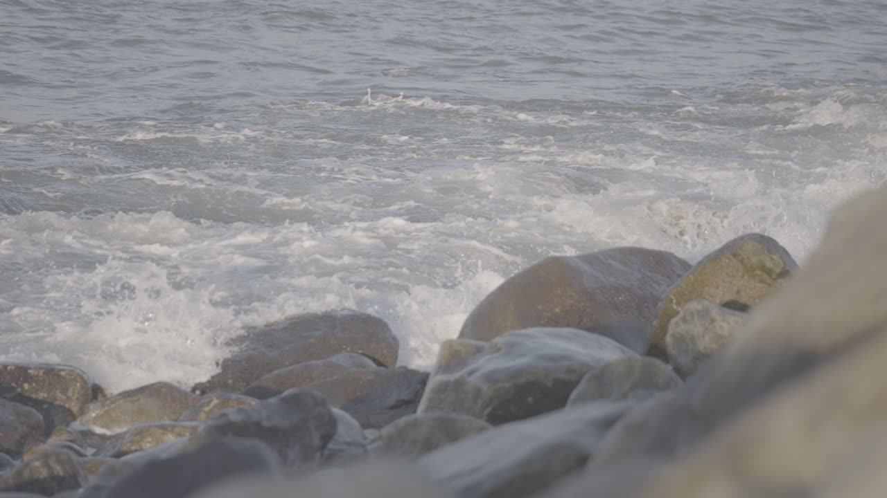 Small waves crashing on the beach near Reve Havn Borestranda Norway during sunset with the beach and sea in the background and the sun reflection in the water with rocks in the foreground LOG