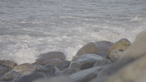 small waves crashing on the beach near reve havn borestranda norway during sunset with the beach and sea in the background and the sun reflection in the water with rocks in the foreground log