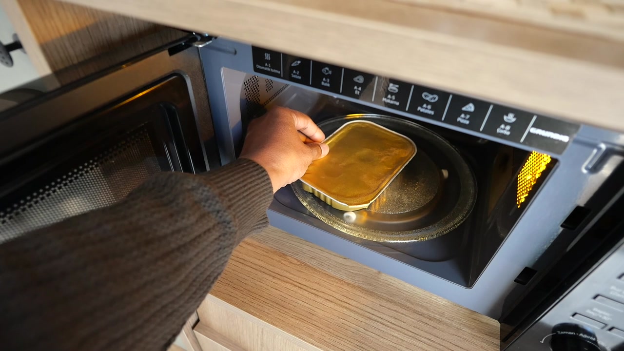 Person's Hand Placing Food Container Inside a Microwave Oven
