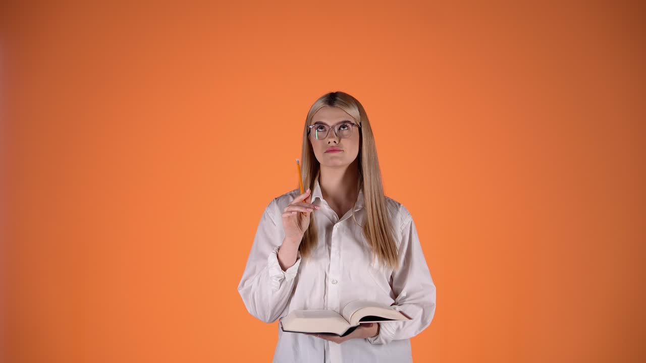 joven rubia pensativa sosteniendo un lápiz y un libro, colorida fotografía de estudio