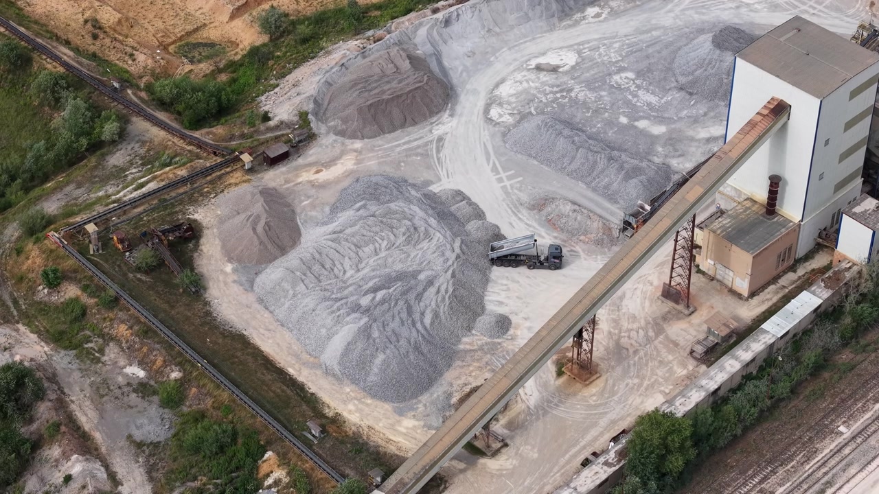 Aerial view of a quarry operation showing a truck being loaded with aggregate near industrial buildings and conveyor systems.