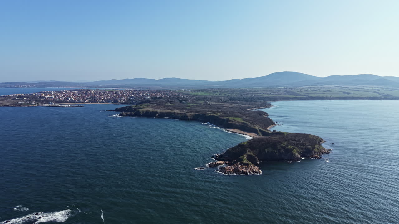 Vista della costa che mostra terra e acqua con colline distanti e un piccolo paese oltre