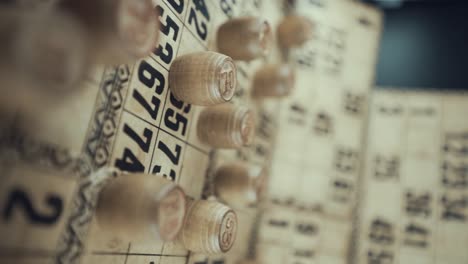 un video macro vertical de un tablero de bingo, luces de estudio, 120 fps, cámara lenta, dígitos de fichas de madera, imágenes en bruto, juego de mesa de lotería vintage, números de cartas, grúa volar por encima de movimiento suave