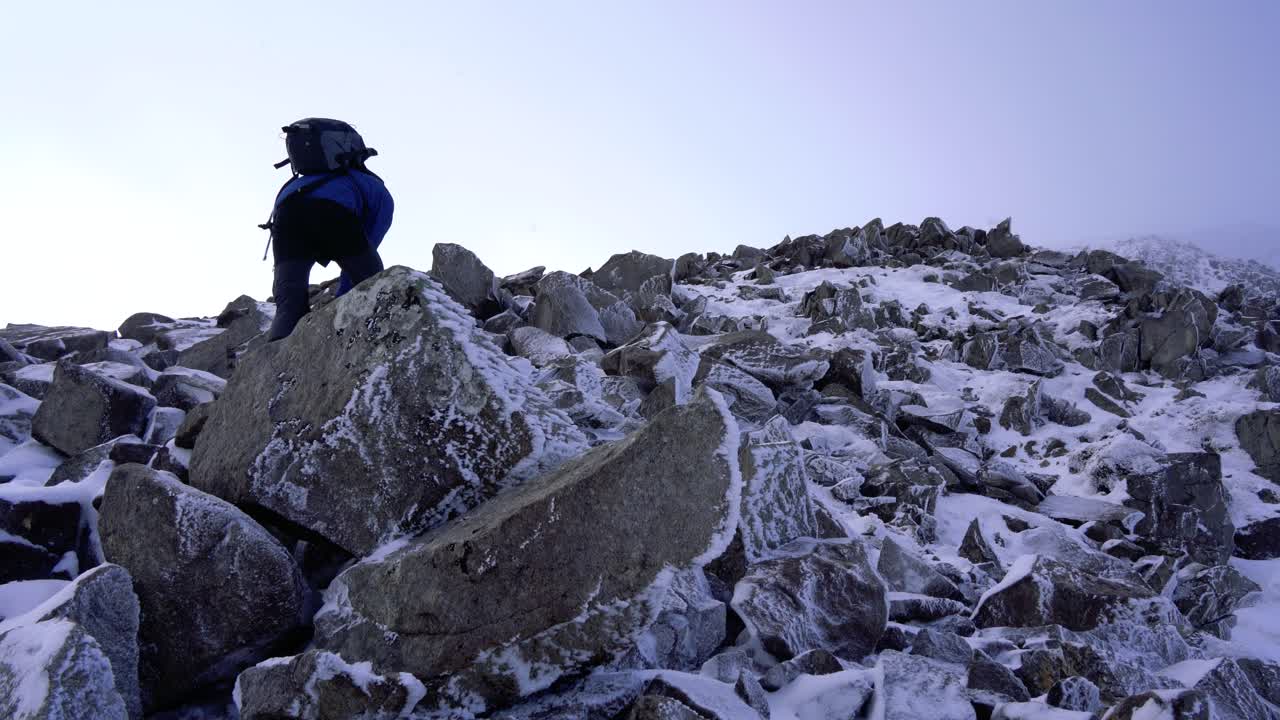 Wandelaar die op een mistige dag over steile rotsen naar de top van een berg klimt