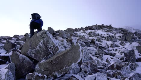 hiker climbing over steep rocks to the summit of a mountain on a foggy day