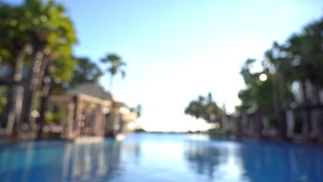 blurred view from inside hotel's outroor lounge swimming pool with tropical palms and rest area