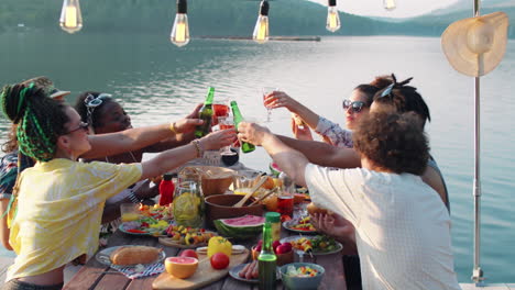 joyous friends clinking glasses in toast at lake party