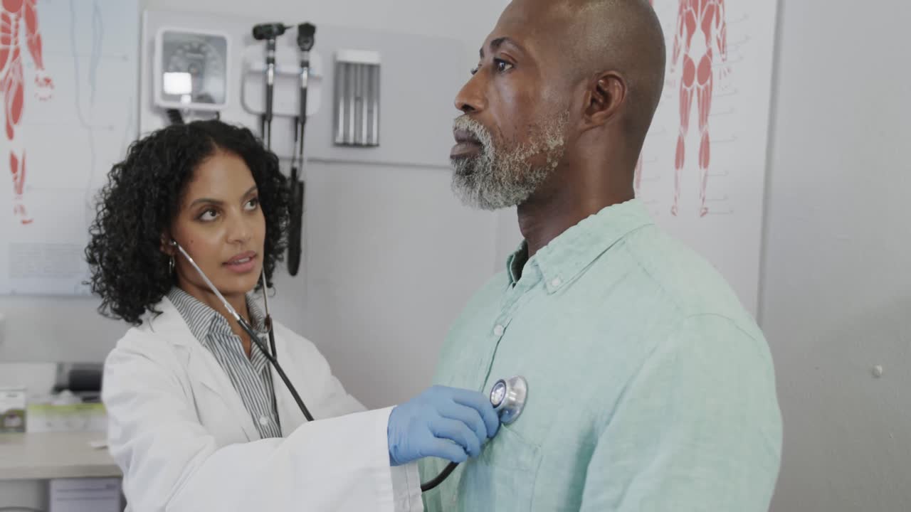 Diverse female doctor examining male patient in consulting room, using stethoscope, slow motion