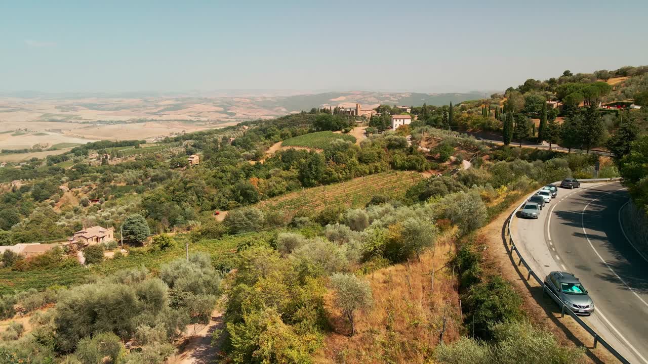 Road adjacent to the Tuscan countryside among the vineyards and olive groves near Montalcino, Italy - aerial drone shot