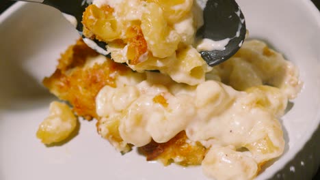 top view of macaroni cheese being placed on plate with serving spoon in slow motion. pasta based main dinner meal dish