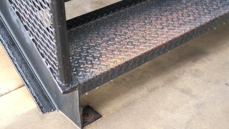 rain dripping slowly off of textured industrial metal cross plate steel staircase outside onto cement ground in slow motion