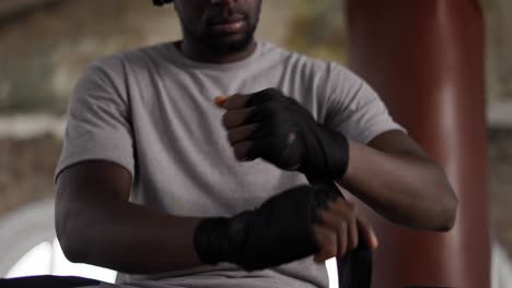 male boxer is wrapping hands with black bandage, close up