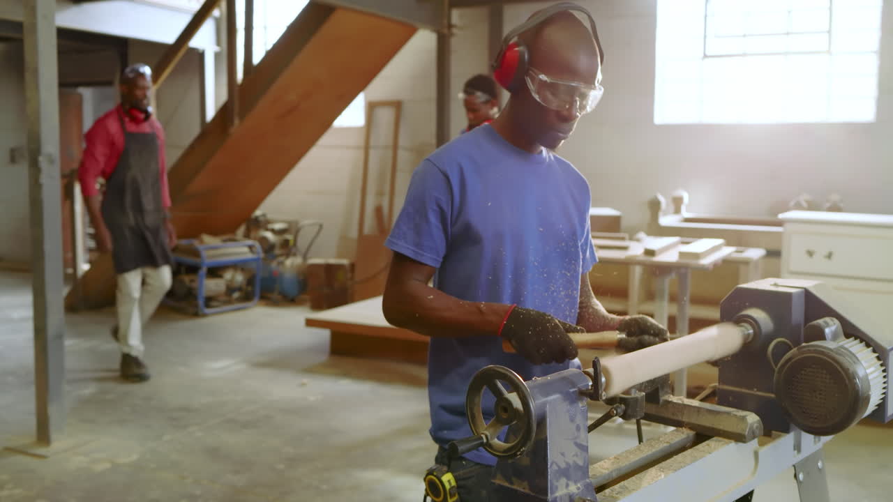 Mid adult African American man powering on lathe carving log after supervisor input at workshop