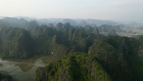 Steile-Gipfel-Von-Kalksteingebirgsketten-Und-Der-Fluss-Ngo-Dong,-Der-In-Einem-Tal-In-Ninh-Binh-Vietnam-Bei-Dunstigem-Sonnenuntergang-Fließt-–-Luftwagen-Links