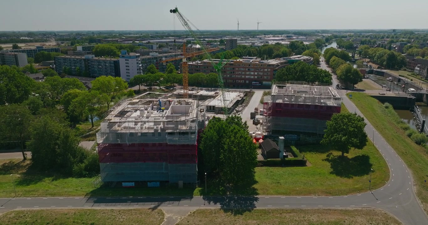 Drone kiertää suurta hollantilaista rakennustyömaata, jossa on nostureita ja uusia kerrostaloja, osoittaen asuinalueen laajenemista ja kaupunkikehitystä asuntopulan ratkaisemiseksi