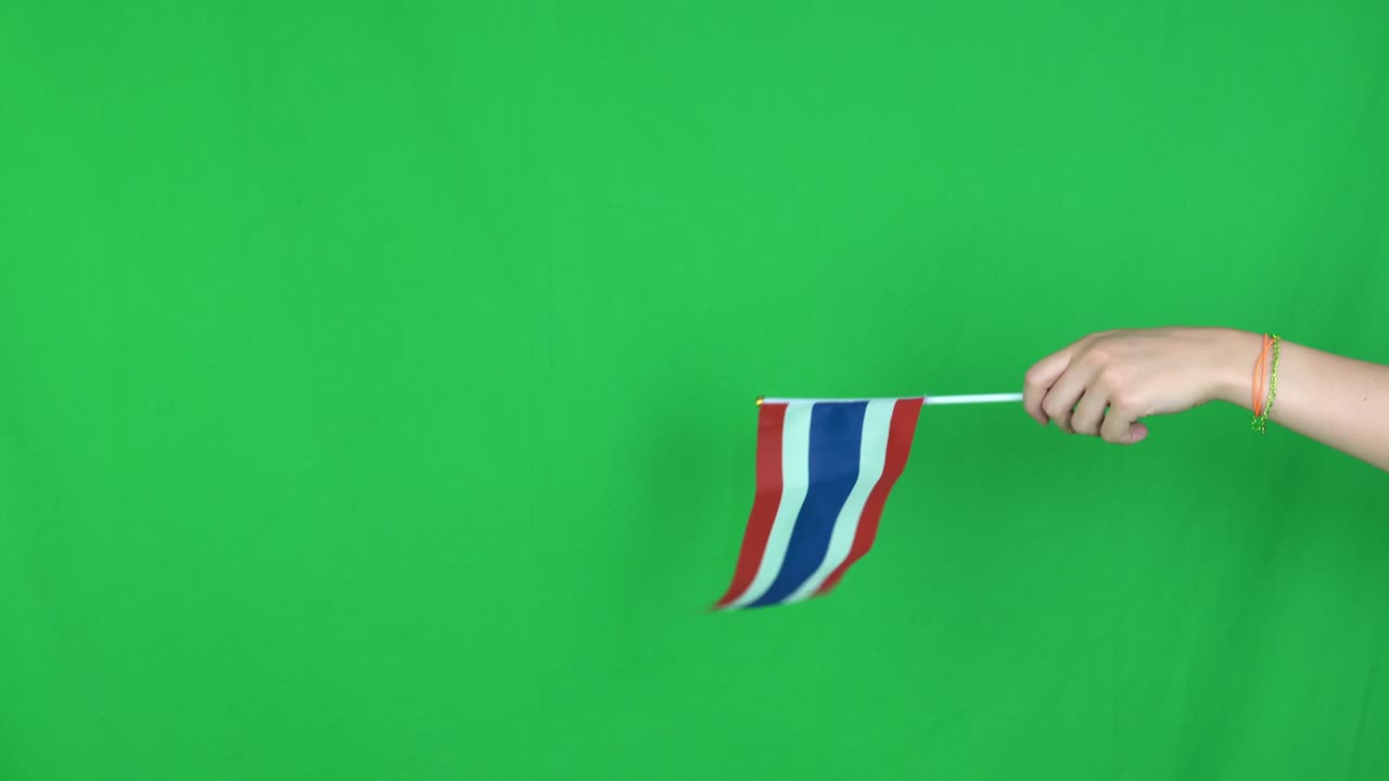 Close up of unknown hand holding a waving Thailand flag on green screen background in the studio.