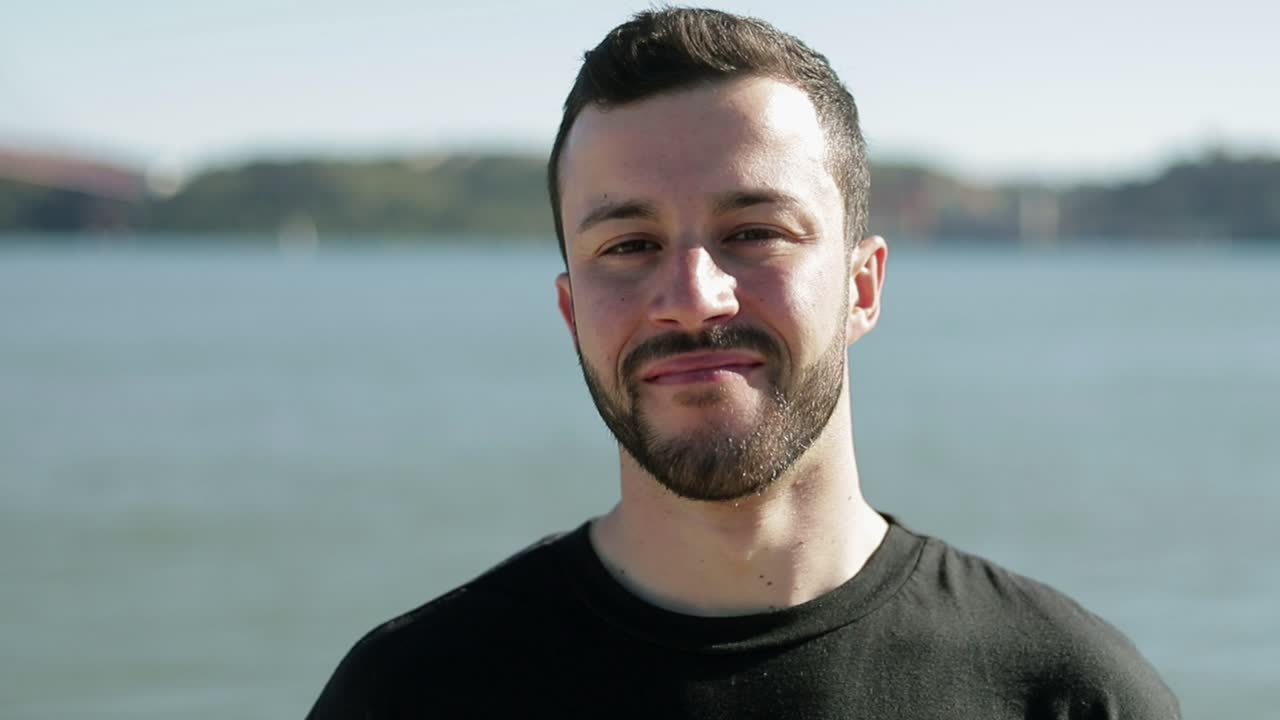 Handsome smiling man wearing black t-shirt posing at riverside.