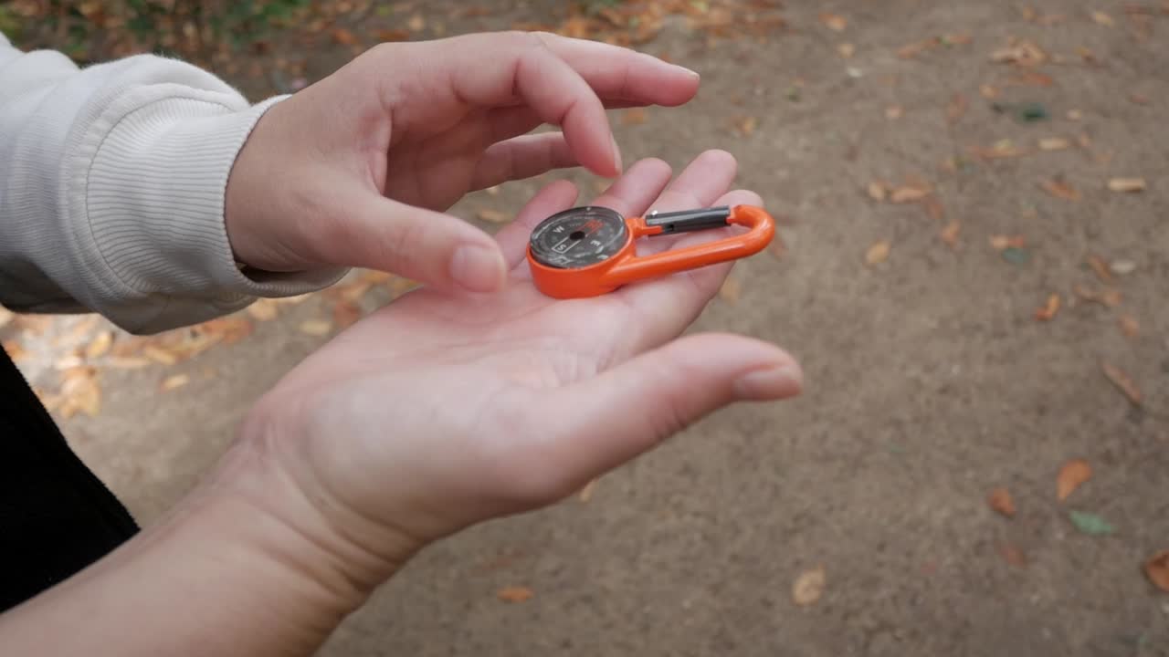 Hand holding an orange compass with a natural outdoor background, symbolizing navigation or adventure