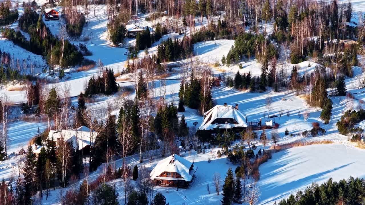 Talvisia vuoristomökkejä lumisessa kohteessa, hirsilukaaleja jäätyneen järven rannalla ilmakuva.