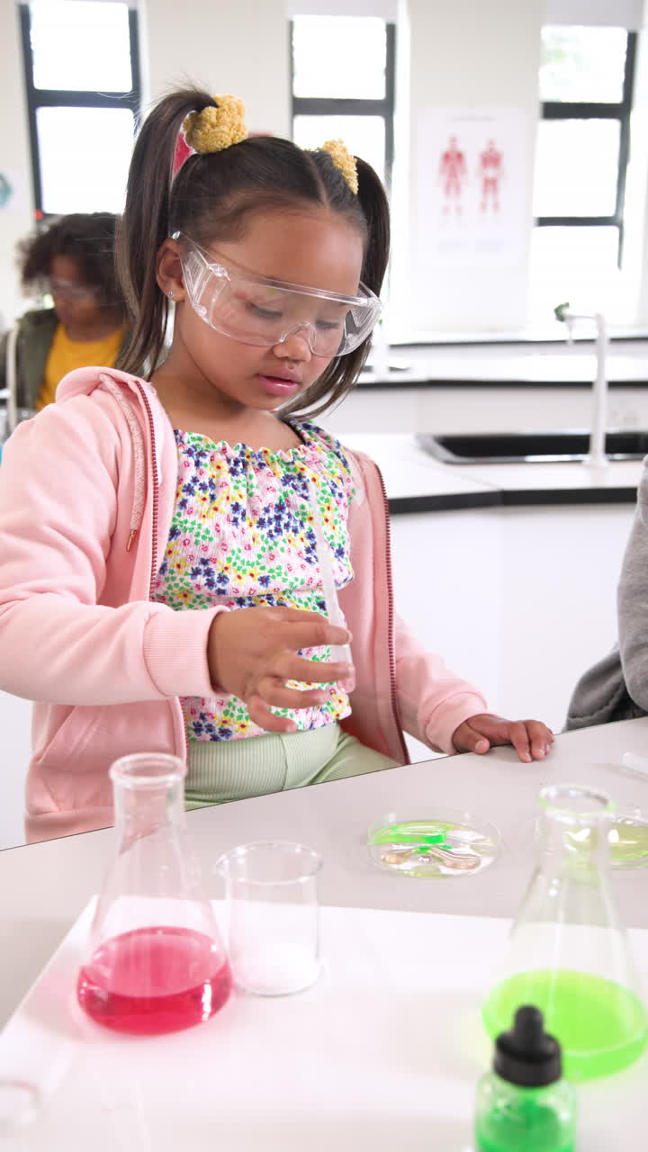 Vertical video: Young girl in science class examining test tube with curiosity and focus