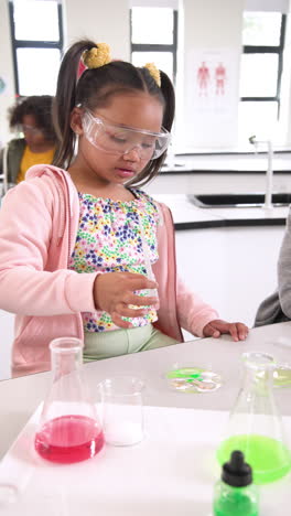 vertical video: young girl in science class examining test tube with curiosity and focus