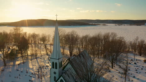 picturesque winter aerial view flying over a small town church and across a frozen river