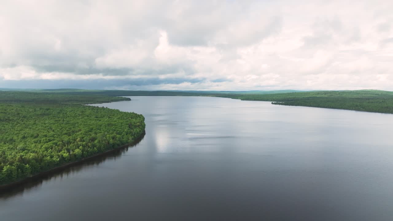 Aerial view over a vast forest and remote lake in Northern Maine. Moody skies, calm waters, and untouched wilderness create a serene, cinematic scene.