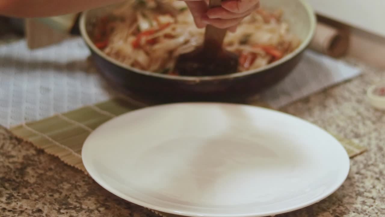 Serving newly cooked stir-fried vegetable rice noodles into a plate showing a candid moment of home cooking and peaceful slow living