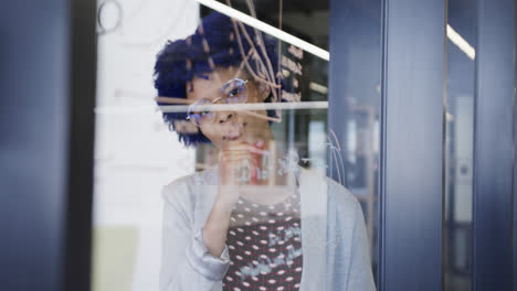 thoughtful biracial casual businesswoman making notes on glass wall, slow motion