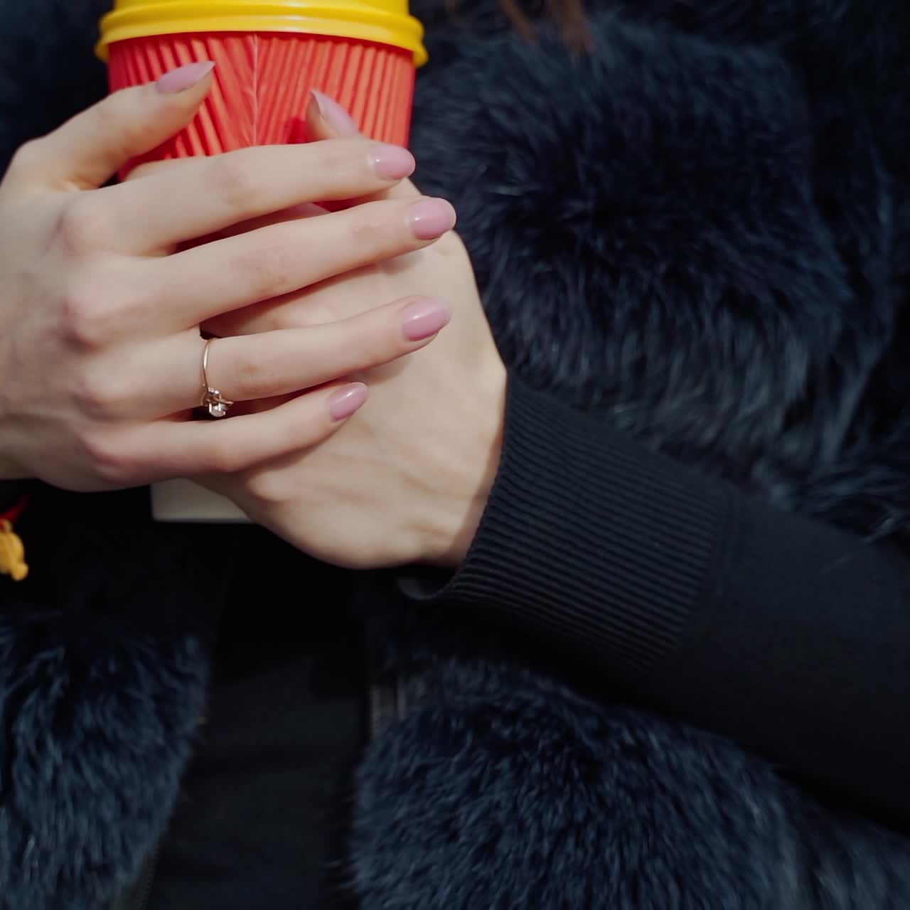 Cup of hot coffee in woman's hands outdoors. Young girl in fur coat warming her hands on the plastic cup with hot drink in a cold season. Close-up.