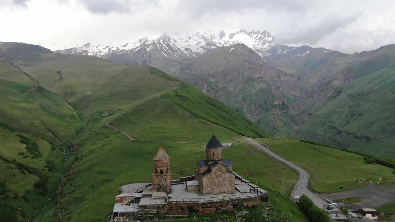 vista aérea de drones en georgia ascender verticalmente gergeti iglesia ortodoxa de la trinidad en kazbegi rodeada de montañas verdes con picos nevados