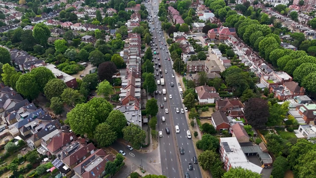 Il traffico scorre lungo un'ampia strada principale tra file di case a schiera e alberi maturi in un sobborgo verdeggiante.